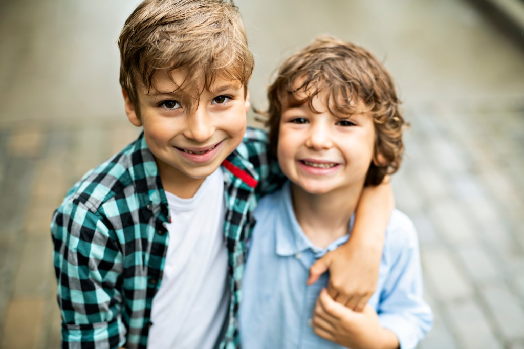 Two smiling brothers hug in a park.