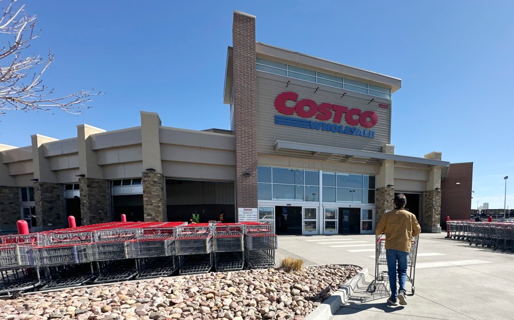 A person pushes a shopping cart towards the entrance of a Costco warehouse.