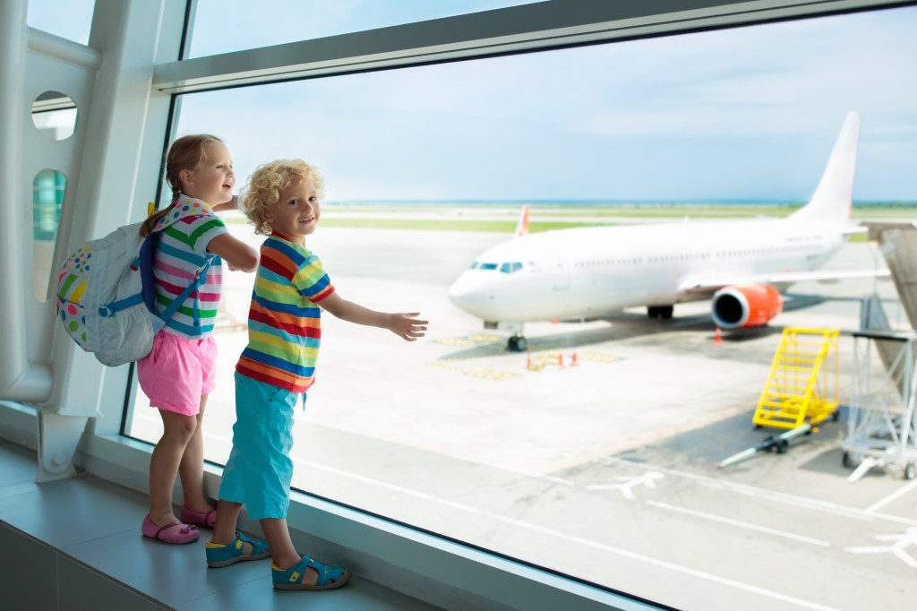 Two children look at an airport window on a plane.